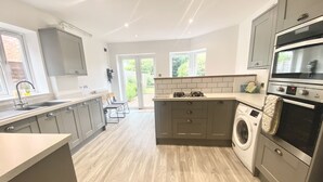 A modern kitchen with grey cabinets, a built-in washing machine, and a large window providing natural light. - Railway Terrace by NewFo rest (Brockenhurst)