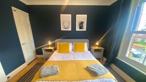 A bedroom with a bed, two bedside tables, a window, and artwork on the wall. - Railway Terrace by NewFo rest (Brockenhurst)