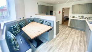 A modern kitchen with grey cabinets, a wooden dining table, and a built-in bench with patterned cushions. - Railway Terrace by NewFo rest (Brockenhurst)