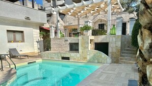 Una piscina con un muro de piedra y una pérgola.