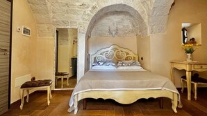 Een slaapkamer met een stenen plafond, een bed met een decoratief hoofdeinde, een nachtkastje en een klein bankje.