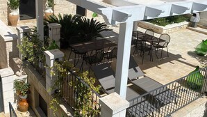 Een terras buiten met een pergola, een zithoek en potplanten.