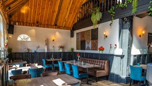 A restaurant interior with wooden ceiling beams, blue upholstered chairs, and a central seating area with a cushioned bench. - Nice Chalet Near the Golf Course in a Holiday Park (Velsen-Zuid)