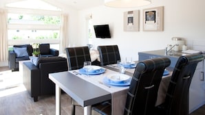 A modern dining area with a table set for two, black leather chairs, a white pendant light, and a kitchen area with a sink and cabinets. - Nice Chalet Near the Golf Course in a Holiday Park (Velsen-Zuid)
