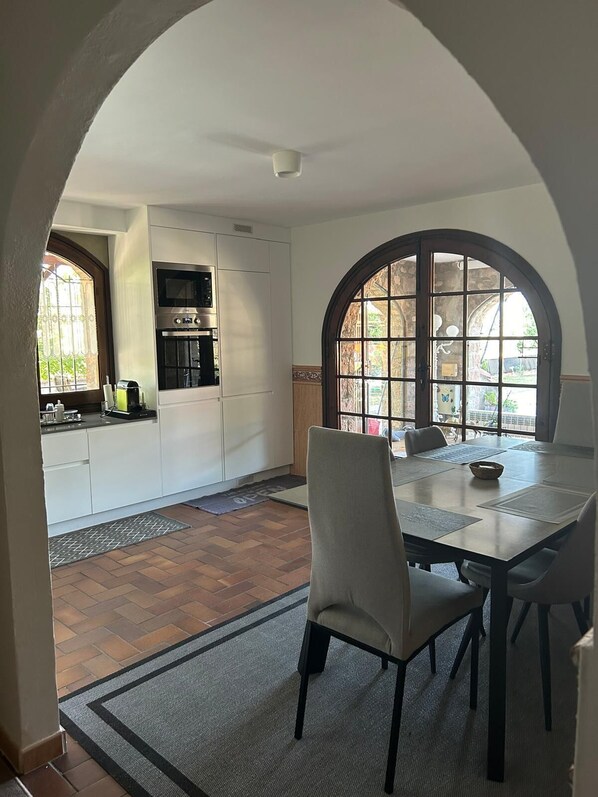 A dining area with a table and chairs, a kitchen with white cabinets and appliances, and a view through an arched window. - Unterkunft Langzeitaufenthalte Wohngegend Guter Verkehrsanbindung 28km von BCN (Canovelles)