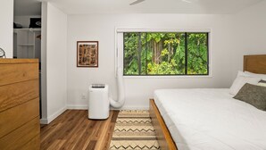 A bedroom with a bed, a ceiling fan, a window with a forest view, a heater, and a wooden dresser. - Summer Deal Princeville 3BR Kauai Townhome with AC and Parking (PRINCEVILLE)