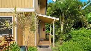 A modern two-story house with a covered porch, surrounded by lush tropical vegetation. - Summer Deal Princeville 3BR Kauai Townhome with AC and Parking (PRINCEVILLE)