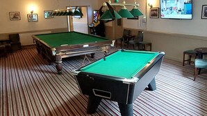 A pool table in a room with striped carpet, a television mounted on the wall, and a ceiling light fixture. - The Cotteridge Inn (Birmingham)