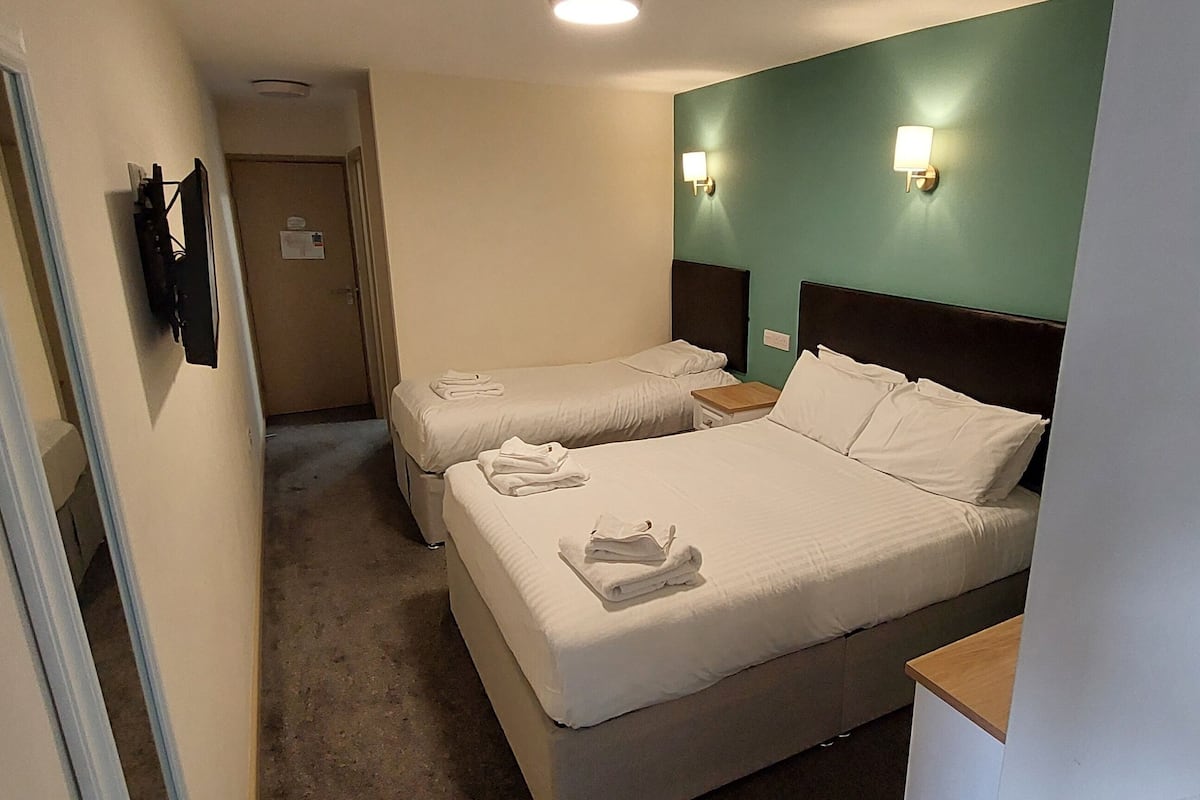 A hotel room with two beds, a flat-screen TV mounted on the wall, and a small wooden side table.