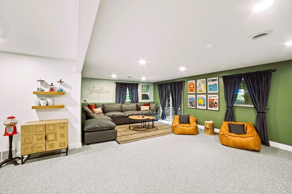 Una sala de estar moderna con un sofá modular, una mesa de centro y un sillón de saco. Hay estanterías con objetos decorativos y una pared con cuadros enmarcados.