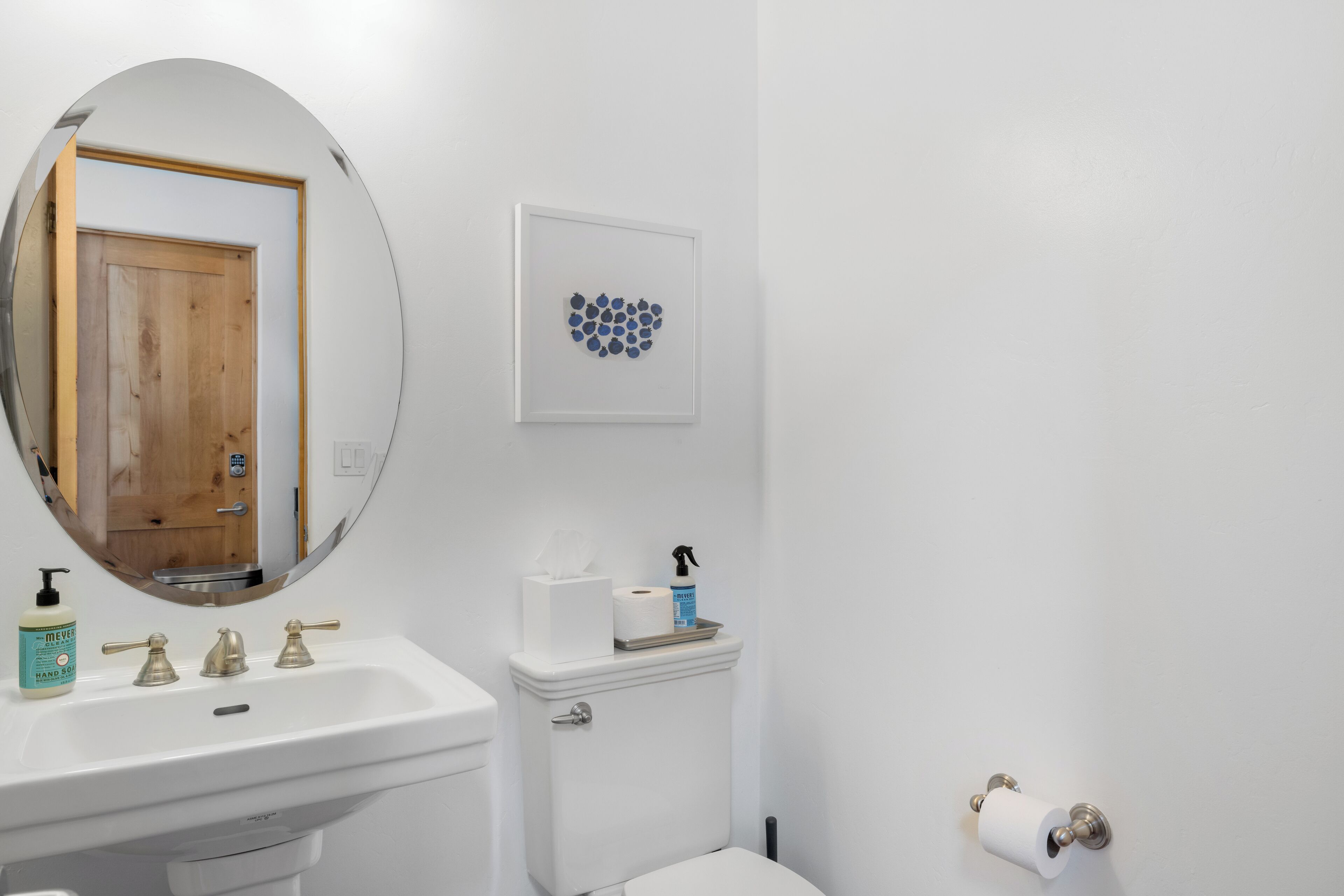 Een badkamer met een wit wastafelmeubel, een spiegel, een toilet en een kunstwerk in een lijst aan de muur.