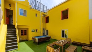 Un bâtiment jaune qui contient une table de billard, des meubles en bois et un escalier.