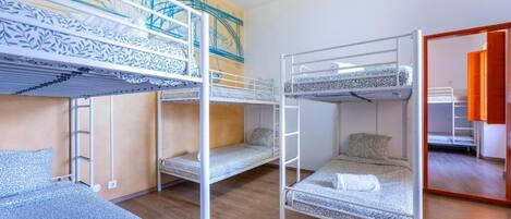 A dormitory room with bunk beds, a wooden floor, and a mural on the wall.