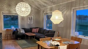 Un salon chaleureux avec un coin repas, un grand lustre et une vue sur l’extérieur.