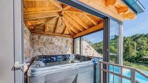 Een hottub met stenen muren en een houten plafond, met uitzicht op een zwembad en een bebost helling.