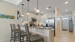 A modern kitchen with a central island, stainless steel appliances, pendant lighting, and a dining area with wooden chairs. - 🌊Incredible Location and Amenities-The Wharf 403🌊 (Orange Beach)