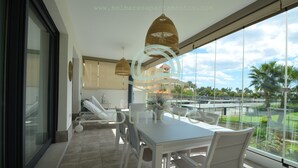 A modern dining area with a table and chairs, a hanging light fixture, and a view of a parking area and greenery. - Los Flamencos 5004 - Two Bedroom Apartment, Sleeps 5 (Punta del moral)