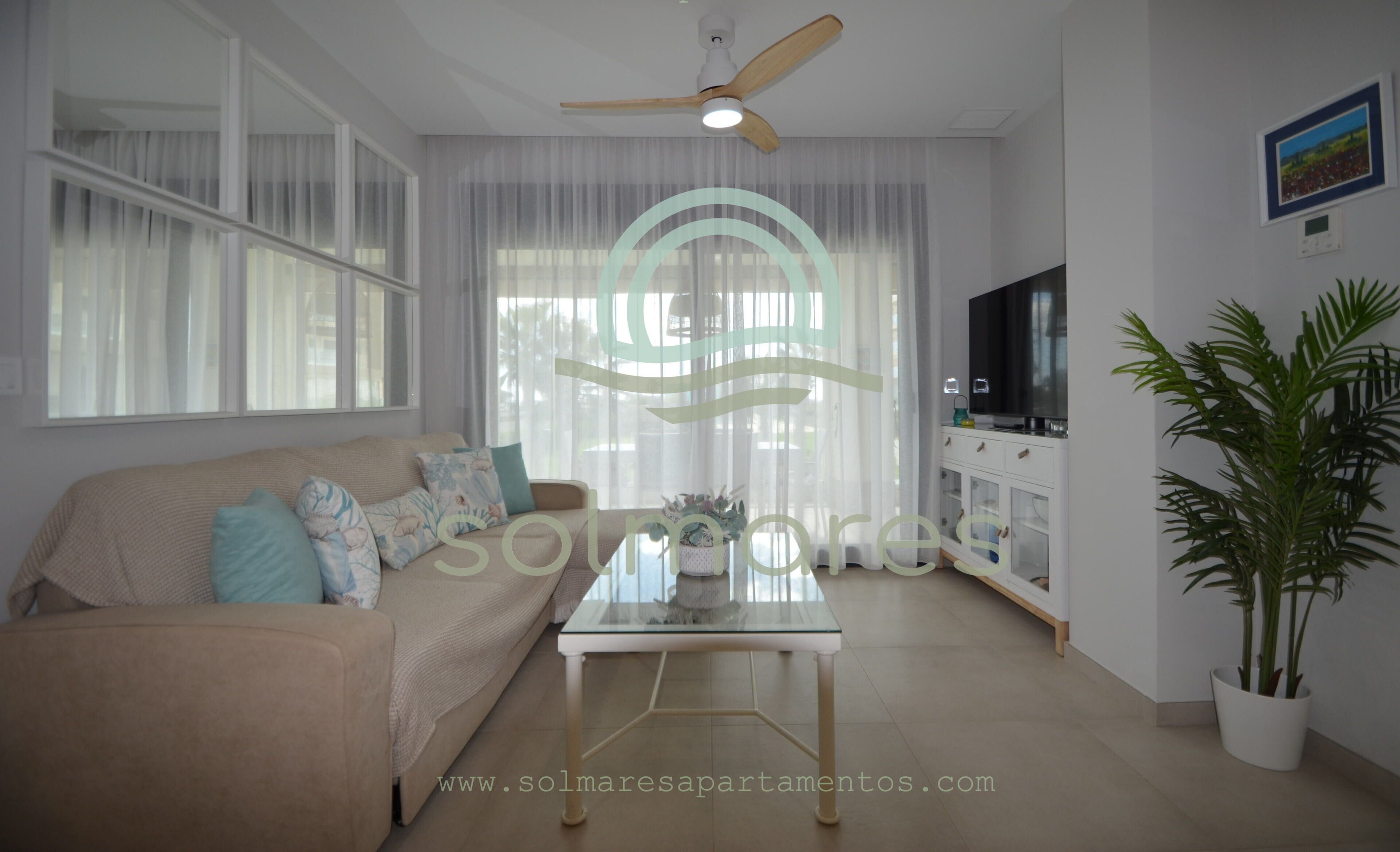 Un salon avec un canapé, une table basse en verre, un ventilateur de plafond, un téléviseur et une plante en pot.