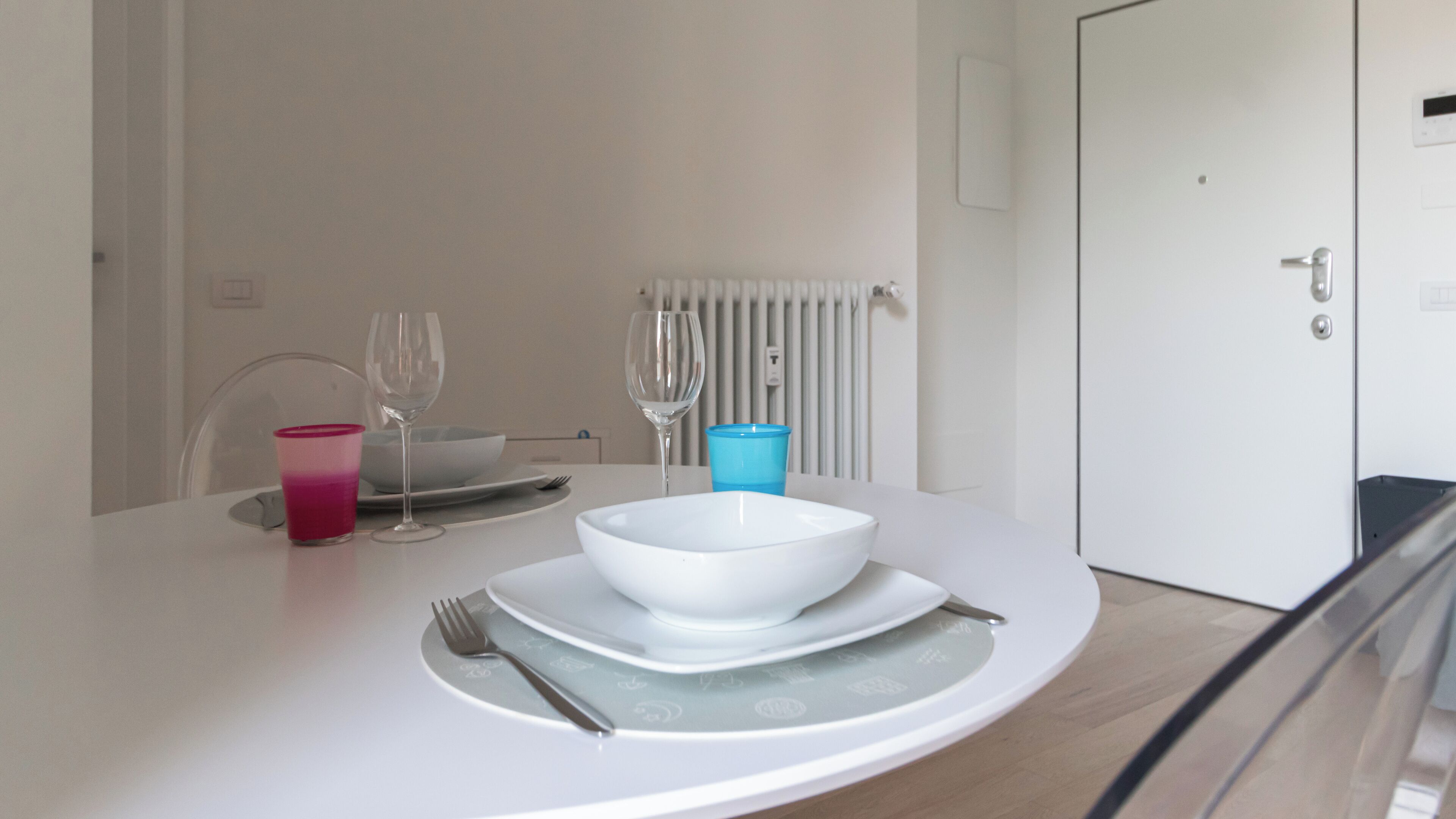 A dining table with a white bowl, a blue cup, and a wine glass.