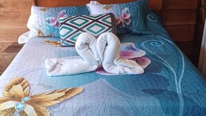 A bed with a blue quilt, floral pillows, and a towel arrangement. - Casa Monstera monteverde 

 (Monte Verde)