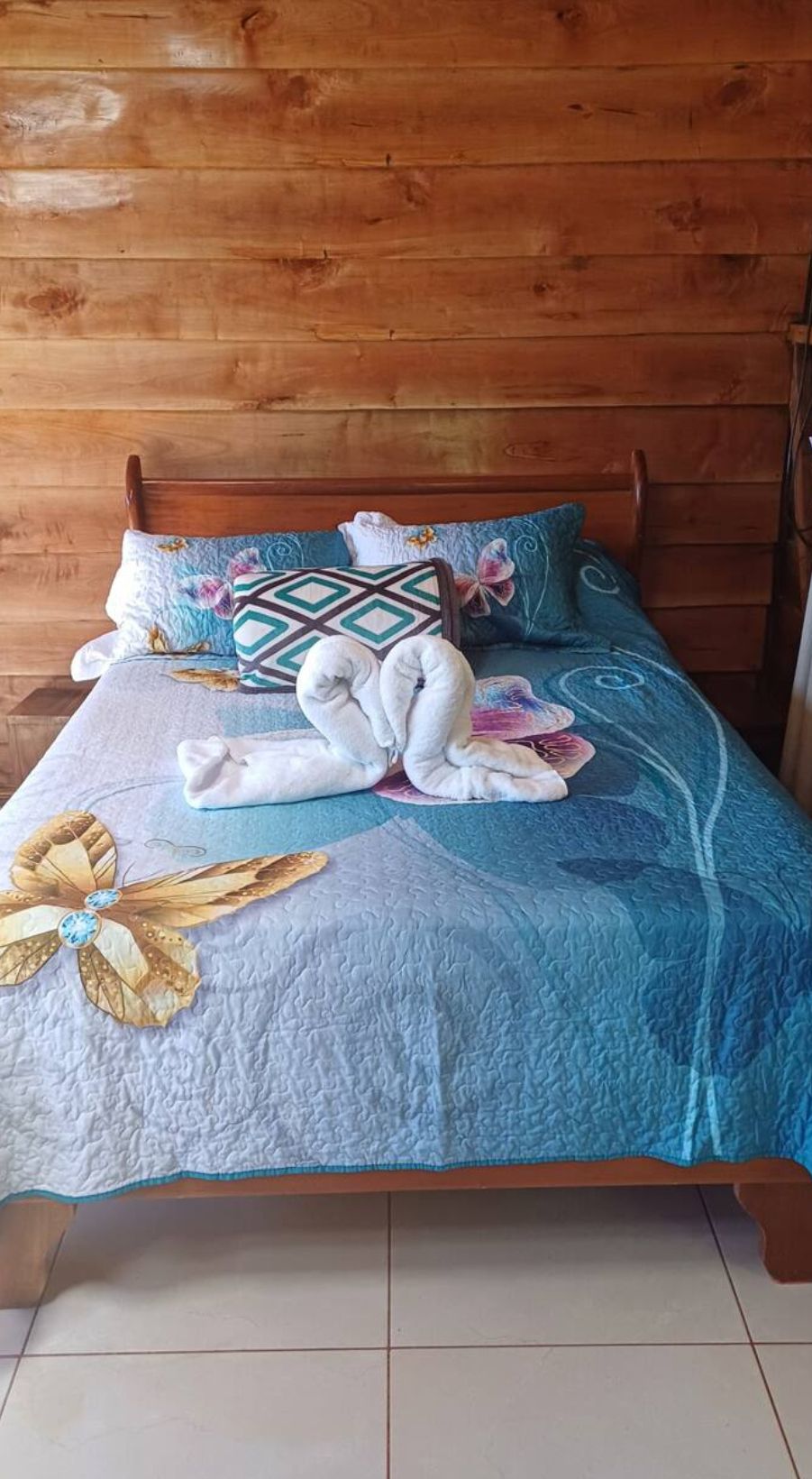 A bed with a blue quilt, floral pillows, and a towel arrangement.