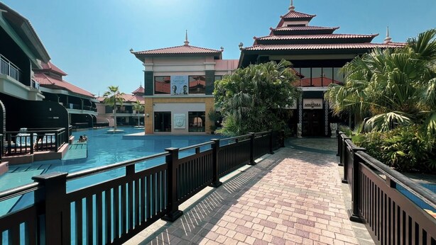 A resort pool area with a tiled walkway, a building with a traditional architectural style, and a sign for 'ANURARA.' - Anantara Palm Ocean View|Beach, Lagoons, Spa & Gym (Dubai)