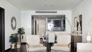 A modern living room with a dining area, featuring a dark wooden coffee table, two beige armchairs, a dining table with chairs, and a kitchen visible through an open doorway. - Anantara Palm Ocean View|Beach, Lagoons, Spa & Gym (Dubai)
