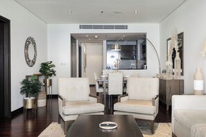 A modern living room with a dining area, featuring a dark wooden coffee table, two beige armchairs, a dining table with chairs, and a kitchen visible through an open doorway. - Anantara Palm Ocean View|Beach, Lagoons, Spa & Gym (Dubai)