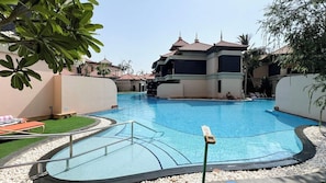 A swimming pool with a surrounding deck, a lifeguard stand, and a building with a tiled roof in the background.