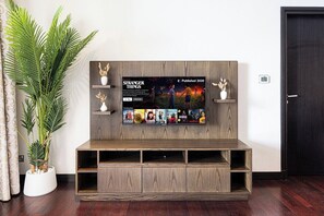 A modern living room with a wooden entertainment unit, a mounted TV displaying a movie poster, and a potted plant.