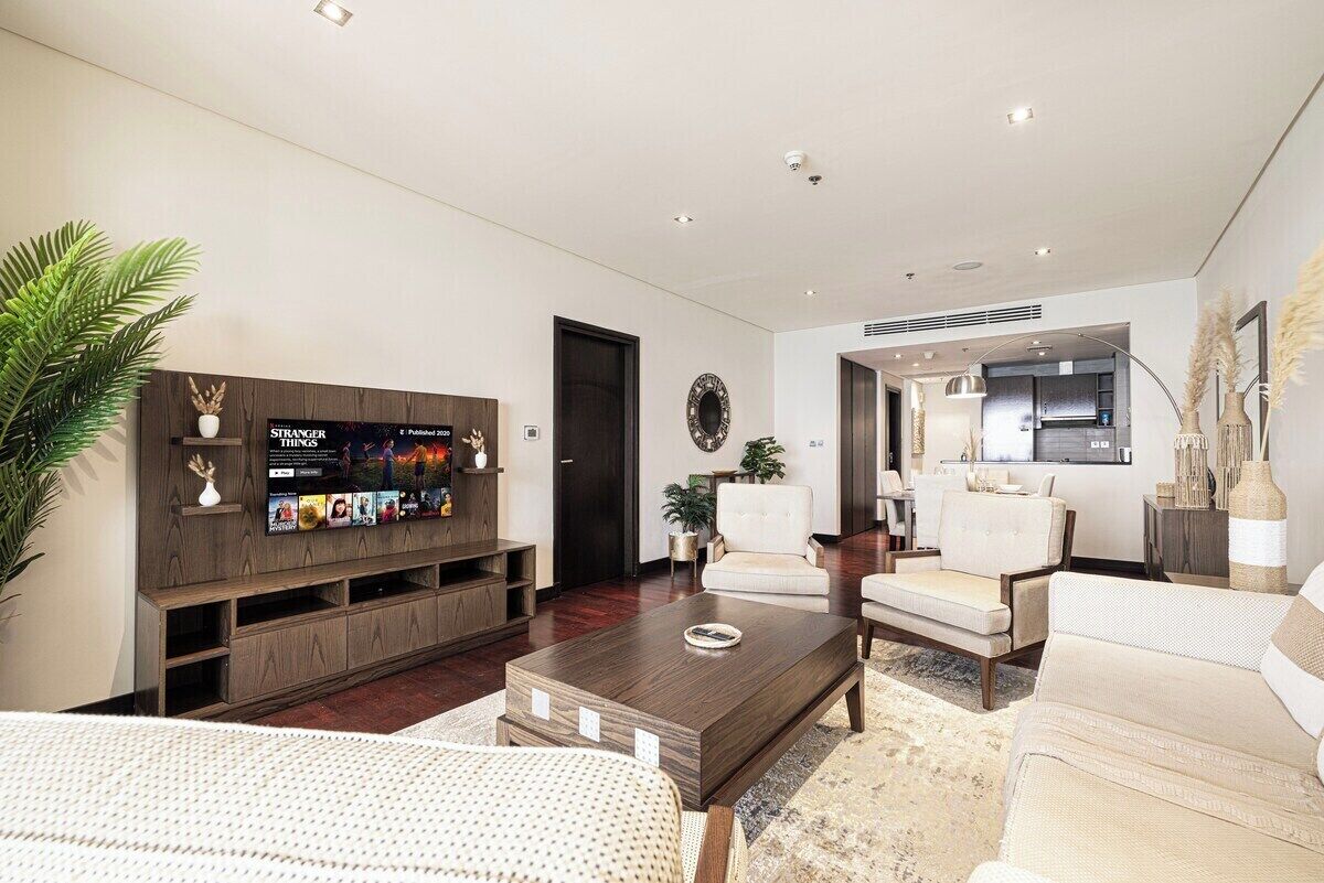 A modern living room with a flat-screen TV, a coffee table, sofas, and a dining area.