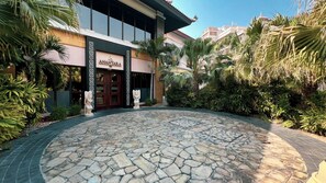 A hotel entrance with a stone-paved courtyard, palm trees, and a statue.