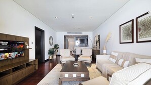 A modern living room with a wooden entertainment unit, a sofa, a coffee table, and a dining area in the background. - Anantara Palm Ocean View|Beach, Lagoons, Spa & Gym (Dubai)