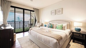 A hotel room with a large bed, a desk, a chair, a balcony with a view of a building, and two framed pictures on the wall. - Anantara Palm Ocean View|Beach, Lagoons, Spa & Gym (Dubai)