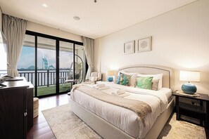 A hotel room with a large bed, a desk, a chair, a balcony with a view of a building, and two framed pictures on the wall. - Anantara Palm Ocean View|Beach, Lagoons, Spa & Gym (Dubai)