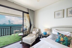 A hotel room with a balcony, a bed with white linens, a nightstand, a chair, and a view of a city skyline. - Anantara Palm Ocean View / Beach / Lagoon Pool (Dubai)