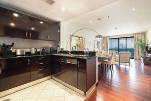 A modern kitchen with dark cabinetry, a central island, and a dining area with a view. - Anantara Palm Ocean View / Beach / Lagoon Pool (Dubai)