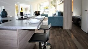 A modern kitchen with a central island, bar stools, and a seating area with a sofa and chairs. - Comfy Chalet With Cooking Island in Limburg (Gulpen)