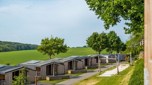 A row of modern, wooden cabins with solar panels, set against a backdrop of green fields and trees. - Comfy Chalet With Cooking Island in Limburg (Gulpen)