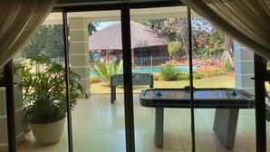 A pool table in a room with a view of a pool and a building with a thatched roof.