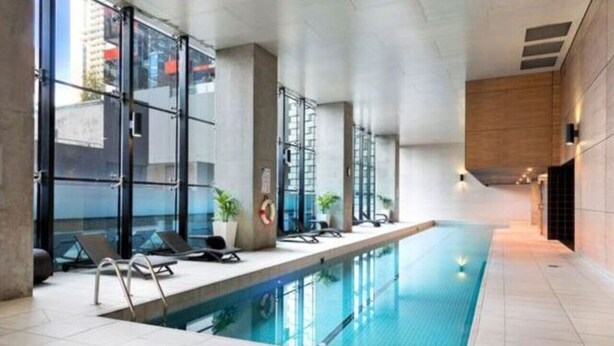 Una piscina interior con paredes de vidrio transparente, sillas de descanso y plantas en macetas.
