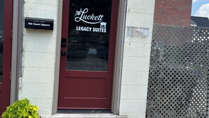 Un immeuble avec une porte rouge, une enseigne indiquant « The Luckett Legacy Suites », et une boîte aux lettres portant le numéro « 102 Court Square ».