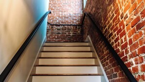 Un escalier avec des marches blanches et des rampes noires, menant à un mur de briques.
