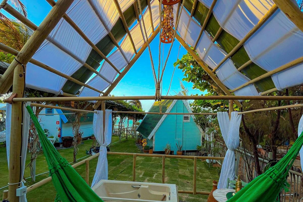 A hammock under a wooden pergola with a view of a house and garden.