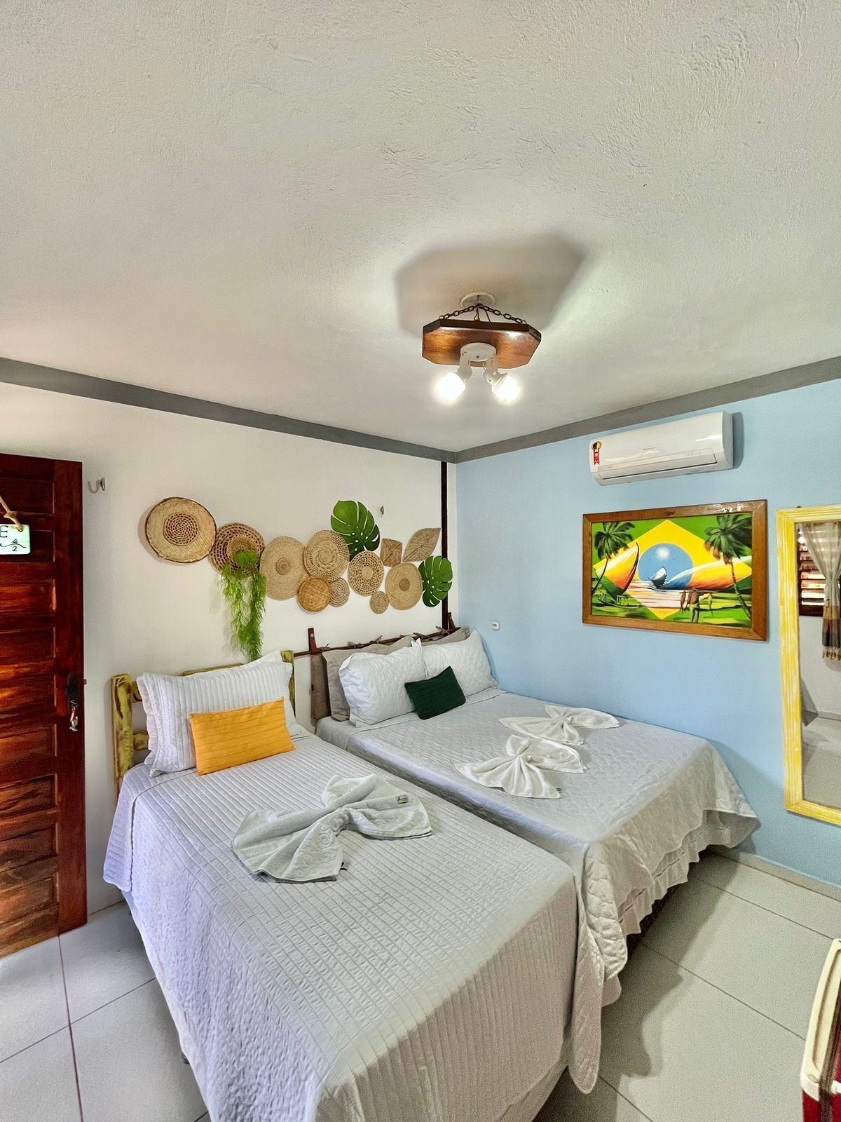 Una stanza con due letti, ventilatore a soffitto, aria condizionata a muro e decorazioni murali.