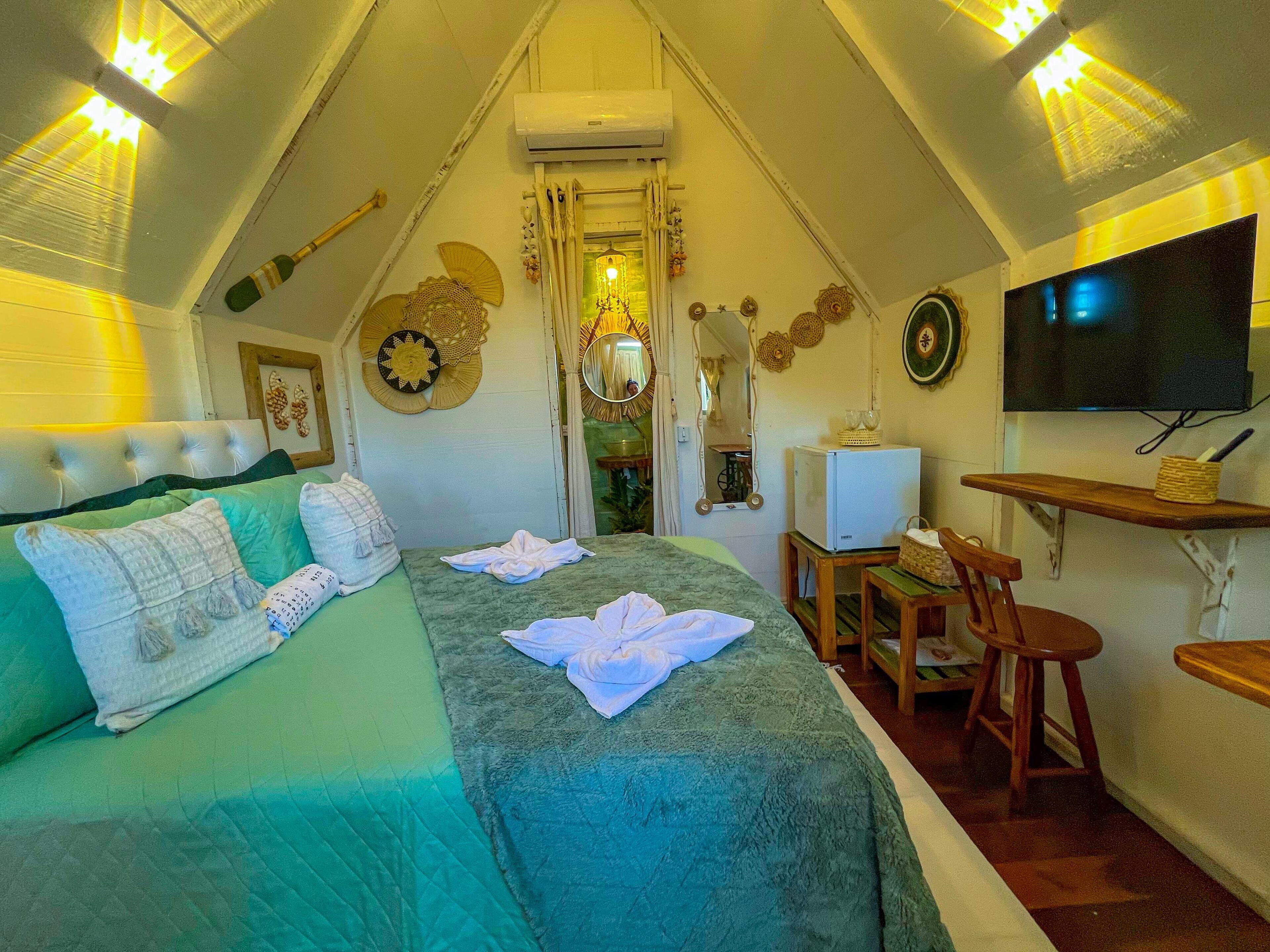 Un dormitorio acogedor y bien iluminado en el ático, con una cama, un escritorio, un televisor y una pequeña mesa.