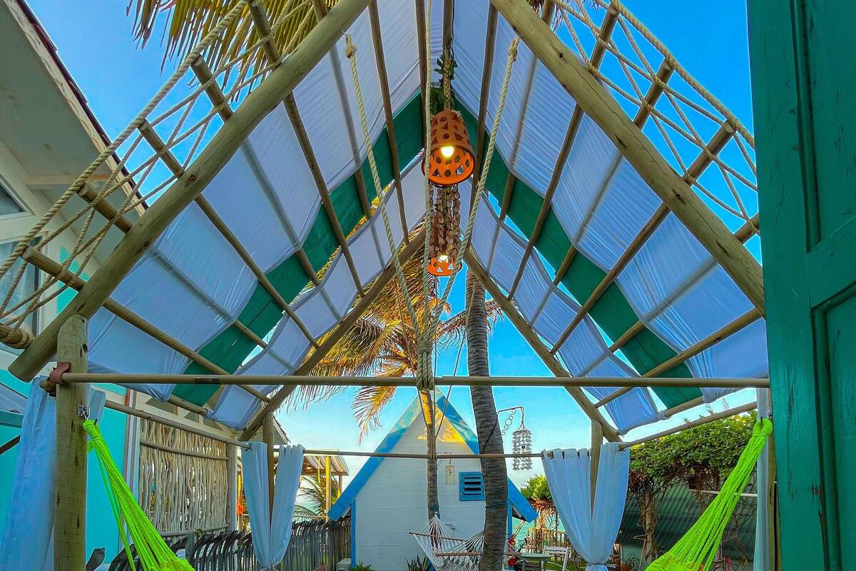 A covered outdoor area with a hammock, wooden seating, and a small garden.