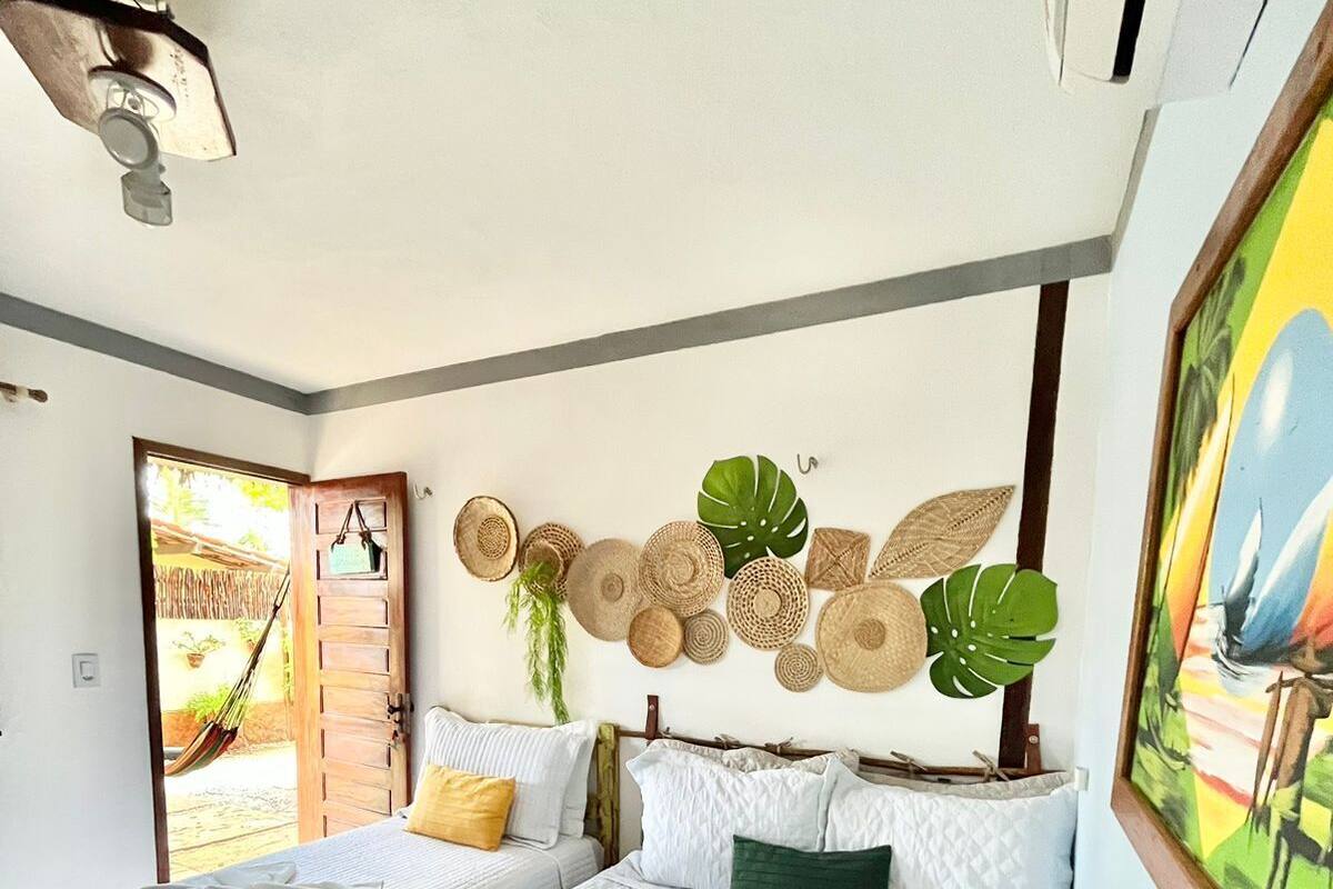 A hotel room with two beds, a ceiling fan, a large window, and a wall decorated with woven baskets and a plant.