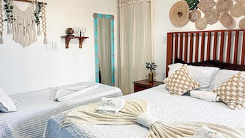 Ein Hotelzimmer mit zwei Betten, einem Holz-Kopfteil, einer Wanddekoration aus Makramee und einem großen Kunstwerk mit einem tropischen Blatt.