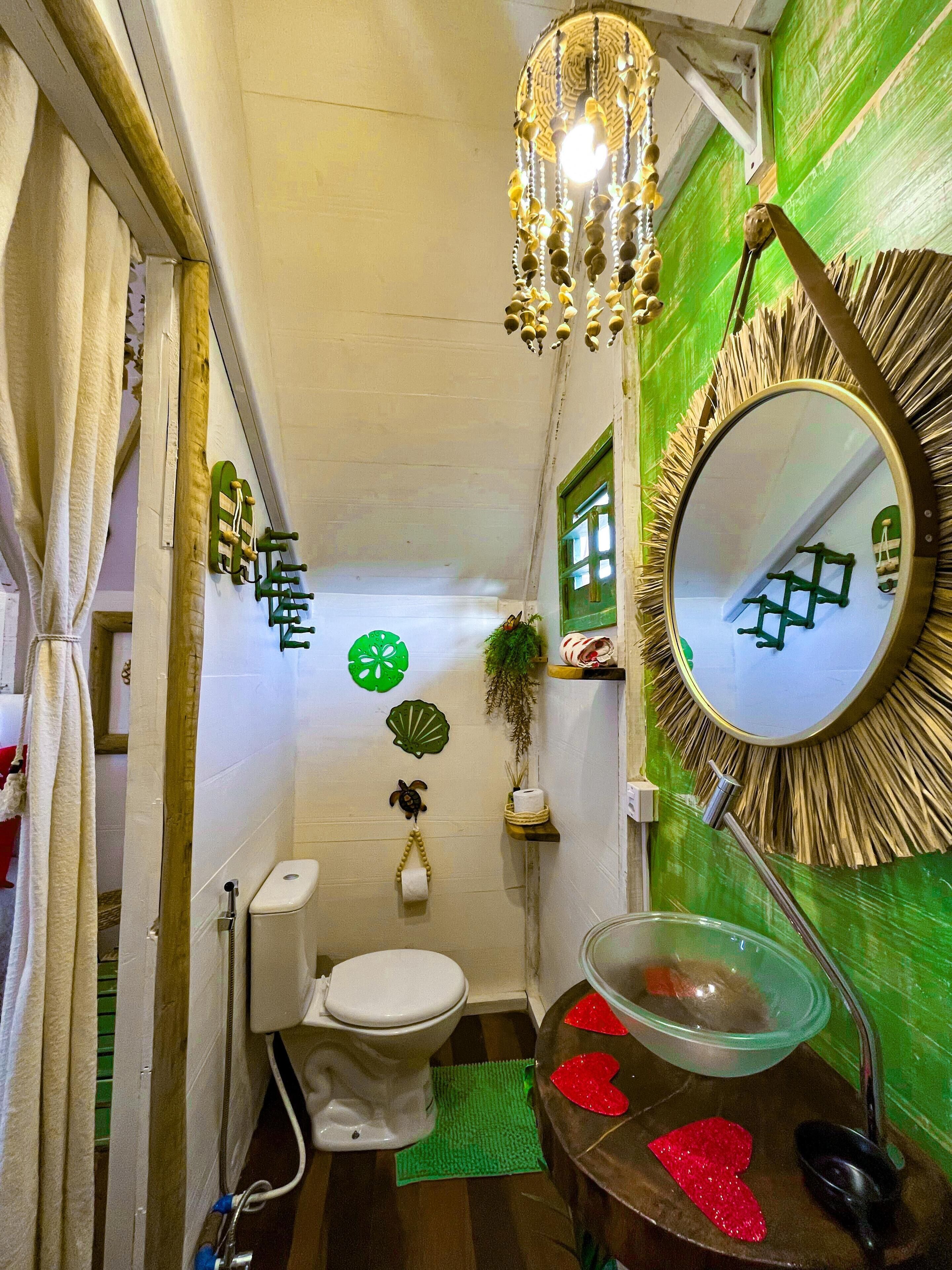 A compact bathroom with a toilet, sink, and mirror. There are decorative elements like a hanging light fixture and wall art.